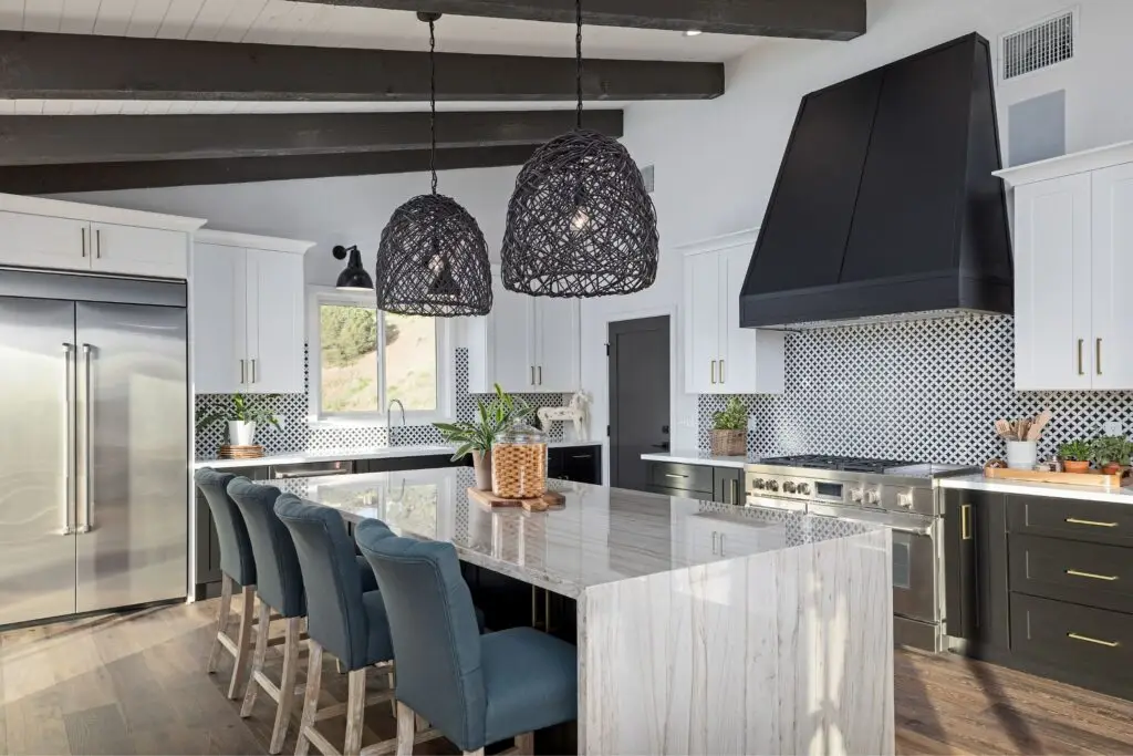 Modern kitchen with a marble island, blue chairs, two large woven pendant lights, stainless steel appliances, and black and white cabinetry—perfect for showcasing in listings managed by an Airbnb agency.