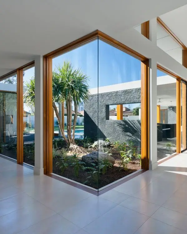 This modern interior, offered through our Airbnb cohosting services, features large glass windows with wooden frames and overlooks an outdoor garden adorned with palm trees and lush greenery.