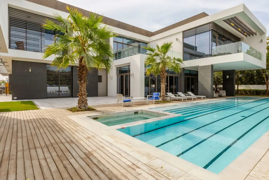 This modern two-story house, available through a premium Airbnb agency, features large windows, a pool, a jacuzzi, and palm trees on a wooden deck. Enjoy the perfect getaway with cohosting services ensuring every detail is taken care of for your comfort.