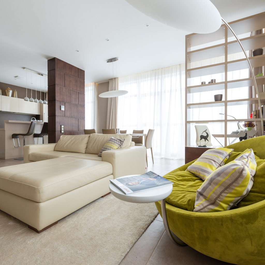 Effortlessly stylish and functional—this modern living space features a cozy beige sectional sofa, inviting green accent chair, sleek open shelving, and a sunlit dining area, all designed to elevate comfort and everyday living.